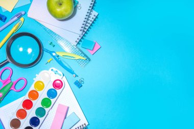 Düz bir zemin, parlak mavi arka planda renkli eğitim malzemeleri vardı. Okul konseptine geri dönelim. Okul çantasında makas, not defteri, kalem, kalem ve malzeme var. Üst görünüm, üstten kopyalama alanı