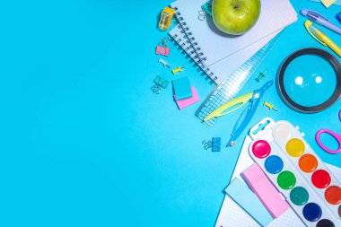 Düz bir zemin, parlak mavi arka planda renkli eğitim malzemeleri vardı. Okul konseptine geri dönelim. Okul çantasında makas, not defteri, kalem, kalem ve malzeme var. Üst görünüm, üstten kopyalama alanı