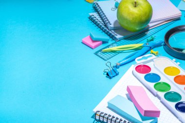 Düz bir zemin, parlak mavi arka planda renkli eğitim malzemeleri vardı. Okul konseptine geri dönelim. Okul çantasında makas, not defteri, kalem, kalem ve malzeme var. Üst görünüm, üstten kopyalama alanı