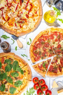 Evde ya da restoranda servis edilen üç çeşit pizza. İçinde pişirme malzemeleri, domates, fesleğen, ıspanak, roka klasik pepperoni pizza, vejetaryen sebze ve deniz ürünleri karidesli pizza var., 