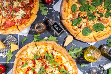 Evde ya da restoranda servis edilen üç çeşit pizza. İçinde pişirme malzemeleri, domates, fesleğen, ıspanak, roka klasik pepperoni pizza, vejetaryen sebze ve deniz ürünleri karidesli pizza var., 