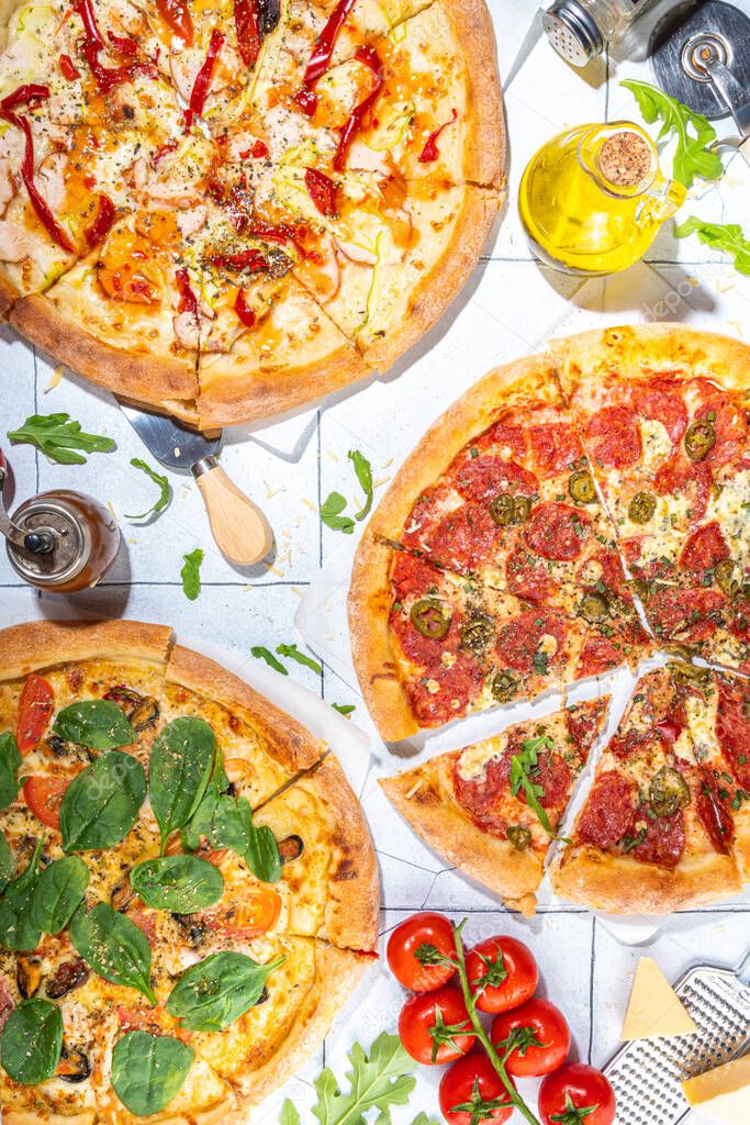 Three various pizzas, served at home or in restaurant on tiled table with cooking ingredients, tomato, basil, spinach, arugula Classic pepperoni pizza, vegetarian vegetable and seafood shrimp pizza, 