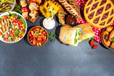 Çeşitli piknik barbekü yemekleri ve flatlay içiyorlar. Yaz bbq piknik yemekleri, ızgara etler, kebaplar, sebzeler, meyve salatası, geleneksel piknik pastası, sandviçler, üst görünüm fotokopi alanı.