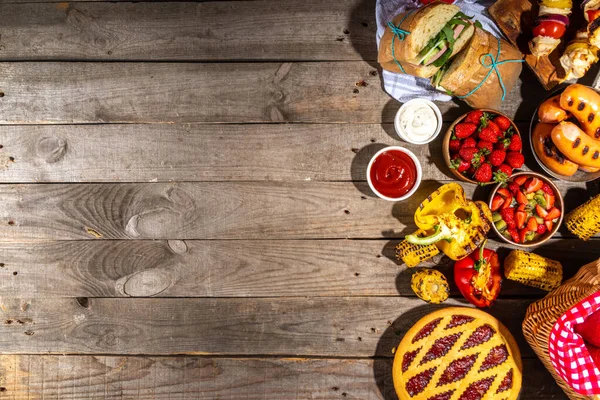 Various picnic barbeque food and drink flatlay. Summer bbq picnic food, assorted grilled meats, kebabs, vegetable, fruit salad, traditional picnic summer pie cake, sandwiches, top view copy space