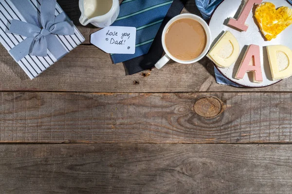 Father day breakfast sandwiches and scrambled eggs.Homemade father day bacon cheese toasts sandwiches with lettering I love dad, with coffee latte cup, gift box and necktie top view copy space