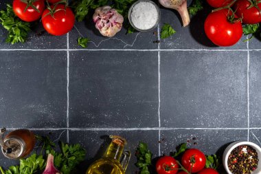 Yemek malzemeleri arka planında. Baharat, karabiber, sarımsak, soğan, yeşillik, domates. Siyah fayanslı masa üzerindeki zeytinyağı fotokopi alanı. Hazırlık sağlıklı gıda geçmişi.