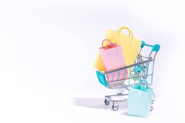 Satış ve alışveriş konsepti. Beyaz arka planda bir sürü pastel renkli alışveriş torbası olan alışveriş arabası oyuncağı dekoru.