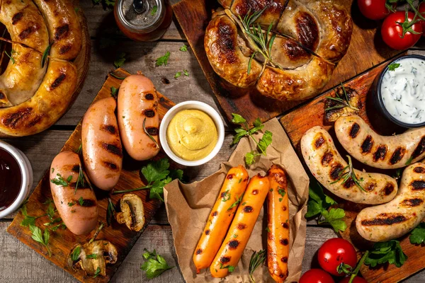 Bavyera sosisi, yuvarlak, gumberland, ketçaplı sucuk, hardal barbekü sosu. Çeşitli bbq ızgara sosisler ahşap arka planda yatıyordu. Sokak festivali ızgara yemek menüsü. 