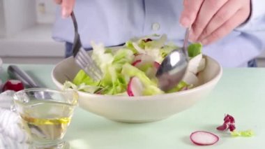 Bahar sebze salatası yapmak marul yaprakları, turplar, taze yeşillikler. Çerçevedeki kız elleri salatayı bir kasede karıştırır. Çerçevedeki kız elleri bitmiş salataya sos ekler.