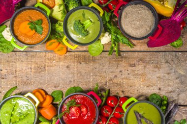 Çeşitli renkte sebze çorbaları. Küçük porsiyonlu kuşkonmaz, ıspanak, brokoli, yeşil bezelye, domates, havuç gibi çeşitli sebze kremalı çorbalar. Ahşap arkaplan kopyalama alanı üst görünümü