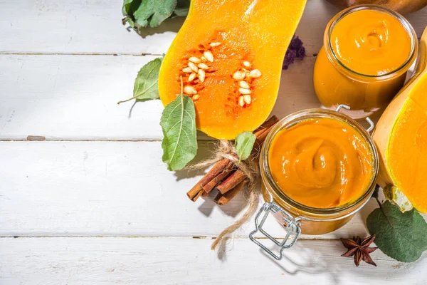 Sweet pumpkin pie jam. Homemade confiture with pumpkin puree and traditional autumn spices. cinnamon, anise. With fresh butternut squash and fall leaves on white wooden background