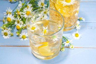 Bitkisel organik soğuk içecek. Çiçek suyu. Buzlu papatya çayı veya limon dilimi ve buz küplü limonata, iki farklı bardakta, mavi ahşap arka plan fotokopi alanı