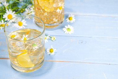 Bitkisel organik soğuk içecek. Çiçek suyu. Buzlu papatya çayı veya limon dilimi ve buz küplü limonata, iki farklı bardakta, mavi ahşap arka plan fotokopi alanı