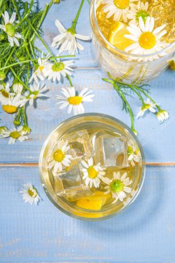 Bitkisel organik soğuk içecek. Çiçek suyu. Buzlu papatya çayı veya limon dilimi ve buz küplü limonata, iki farklı bardakta, mavi ahşap arka plan fotokopi alanı
