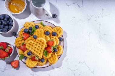 Çilekli, yaban mersinli ve ballı Belçika waffle 'ları, beyaz mutfak masalarında ev yapımı kalp şeklinde waffle' lar.