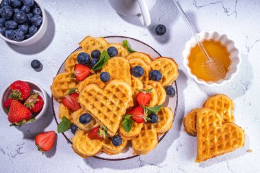 Çilekli, yaban mersinli ve ballı Belçika waffle 'ları, beyaz mutfak masalarında ev yapımı kalp şeklinde waffle' lar.