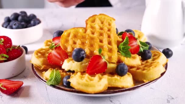 早餐比利时华夫饼与草莓 蓝莓和蜂蜜 自制的健康心脏形状华夫饼与白色厨房桌子复制空间 — 图库视频影像