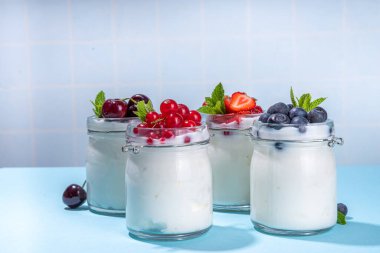 Portakallı cam kavanozlarda çeşitli yoğurtlar. Mevsimlik çilekli, kirazlı, üzümlü, üzümlü sağlıklı yaz kahvaltısı konsepti. 