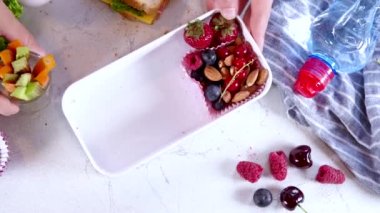 Okula dönelim. Anne kadın elleri çocukların beslenme çantasını taze meyve, yoğurt, sağlıklı sandviç ve sebze atıştırmalıklarıyla dolduruyor. Beyaz mutfak mermer masa kopyası