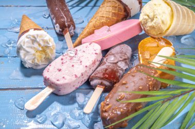 Siyah arka planda çeşitli dondurma setleri. Tahta mavi plaj zemininde buzlu dondurma ve koni çeşitleri ve tropikal palmiye yaprakları üst düz görünüm kopya alanı