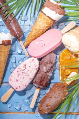 Siyah arka planda çeşitli dondurma setleri. Tahta mavi plaj zemininde buzlu dondurma ve koni çeşitleri ve tropikal palmiye yaprakları üst düz görünüm kopya alanı