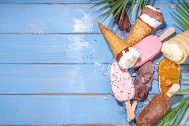 Siyah arka planda çeşitli dondurma setleri. Tahta mavi plaj zemininde buzlu dondurma ve koni çeşitleri ve tropikal palmiye yaprakları üst düz görünüm kopya alanı