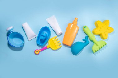 Baby Sunscreen suncare concept. Suntan lotion bottles with kids vacation accessory, sand molds, panama hat, on light blue background copy space