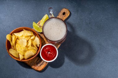 Çeşitli tuzlu abur cuburlarla bira. Siyah masa arkaplanı geleneksel parti atıştırmalıkları, bira şişeleri ve bardaklar, cips, soğan halkaları, tuzlanmış fındık, cips ve soslu üst görünüm fotokopi alanı