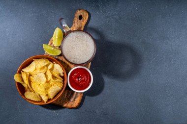 Çeşitli tuzlu abur cuburlarla bira. Siyah masa arkaplanı geleneksel parti atıştırmalıkları, bira şişeleri ve bardaklar, cips, soğan halkaları, tuzlanmış fındık, cips ve soslu üst görünüm fotokopi alanı