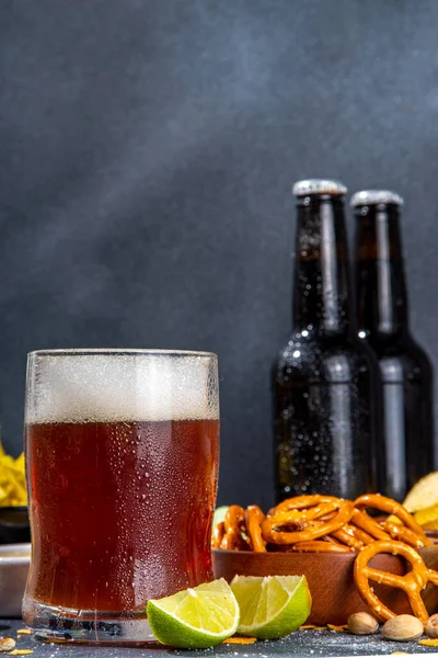 Beer with various salted snacks set. Black table background with traditional party snacks, beer bottles and glasses, with chips, onion rings, salted nuts, crisps and sauces top view copy space