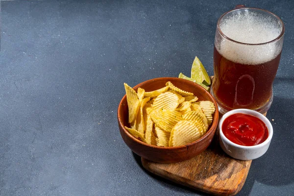 Beer with various salted snacks set. Black table background with traditional party snacks, beer bottles and glasses, with chips, onion rings, salted nuts, crisps and sauces top view copy space