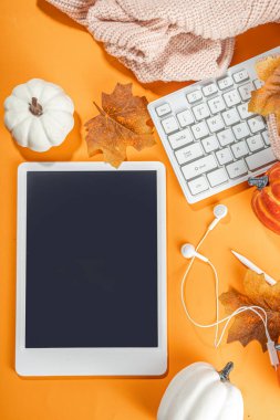 Tablet, kulaklık, beyaz, turuncu balkabağı ve turuncu arka planda sonbahar yaprakları olan samimi bir sonbahar arkaplanı. Sonbahar durgun yaşam kompozisyonu. 