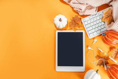 Tablet, kulaklık, beyaz, turuncu balkabağı ve turuncu arka planda sonbahar yaprakları olan samimi bir sonbahar arkaplanı. Sonbahar durgun yaşam kompozisyonu. 