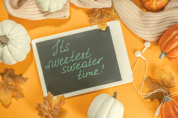 Cozy fall background with tablet, ear-pods, white, orange pumpkins, autumn leaves decor on high-colored orange background. Autumn still life composition.