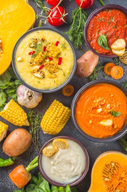 Farklı sonbahar çorbaları seti. Portakal kaselerinde çeşitli sebze çorbaları - mısır, patates, balkabağı, domates, kabak, brokoli kremalı çorba. Siyah beton arkaplanda üst görünüm kopyalama alanı