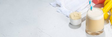 Beyaz vanilyalı beyaz protein karıştırma bardağı, saman, protein tozu, dambıl, havlu ve fitness aksesuarları ile beyaz spor bar arka planında fotokopi alanı