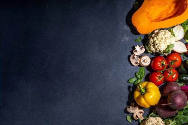 Autumn vegetables cooking background. Organic fall harvest farm vegetables, mushrooms. Various vegetarian ingredients set for cooking dinner on black kitchen background, top view copy space