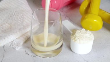 Vanilla white protein shake glass, with straw, with protein powder, dumbbell, towel and fitness accessories, on white sport bar table background 