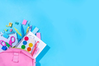Düz bir zemin, parlak mavi arka planda renkli eğitim malzemeleri vardı. Okul konseptine geri dönelim. Okul çantasında makas, not defteri, kalem, kalem ve malzeme var. Üst görünüm, üstten kopyalama alanı