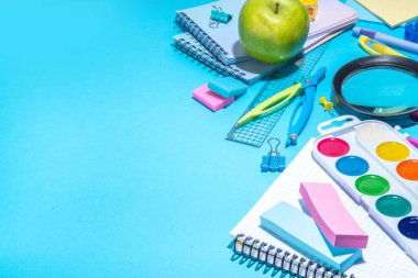 Düz bir zemin, parlak mavi arka planda renkli eğitim malzemeleri vardı. Okul konseptine geri dönelim. Okul çantasında makas, not defteri, kalem, kalem ve malzeme var. Üst görünüm, üstten kopyalama alanı