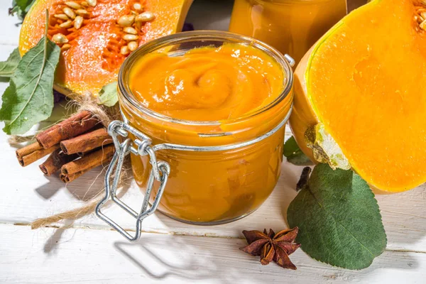 Sweet pumpkin pie jam. Homemade confiture with pumpkin puree and traditional autumn spices. cinnamon, anise. With fresh butternut squash and fall leaves on white wooden background