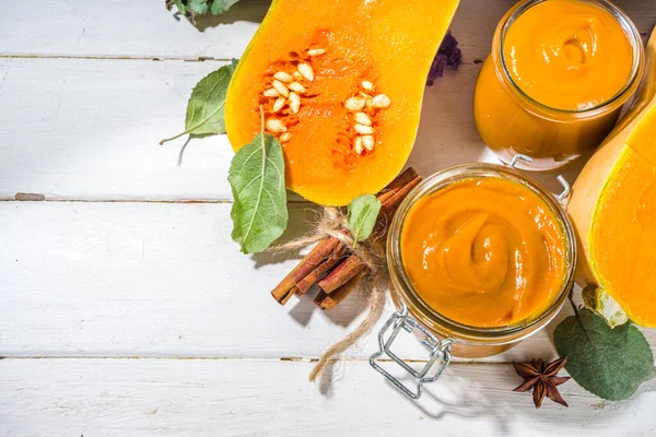 Sweet pumpkin pie jam. Homemade confiture with pumpkin puree and traditional autumn spices. cinnamon, anise. With fresh butternut squash and fall leaves on white wooden background