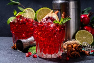 Spicy autumn pomegranate cocktail. Alcohol warming gin drink with pomegranate, lime, cinnamon, mint, autumn winter sangria on dark background copy space