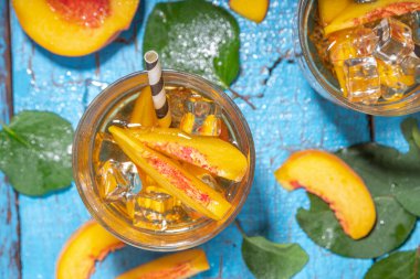 Homemade peach ice tea with ripe fresh peaches on high-colored blue wooden background