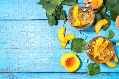 Homemade peach ice tea with ripe fresh peaches on high-colored blue wooden background