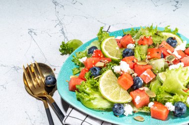 Summer watermelon salad. Fresh raw green salad with lettuce, arugula, watermelon slices, blueberry, feta cheese and honey
