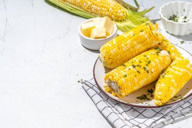 Boiled corn with butter and herbs. Ripe yellow organic cooked corn cobs, on a white kitchen table