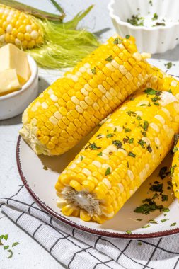 Boiled corn with butter and herbs. Ripe yellow organic cooked corn cobs, on a white kitchen table
