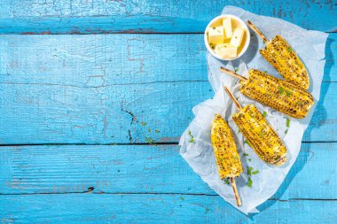 Sweet corn grilled with butter, cheese, cilantro and herbs. Vegetarian, healthy, clean eating barbeque food. Portioned bbq grill corn cobs on high-colored blue wooden background