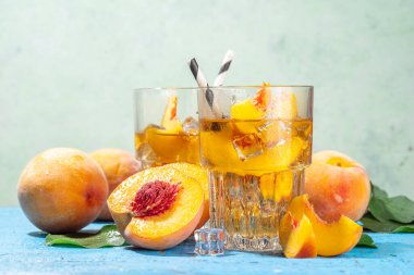 Homemade peach ice tea with ripe fresh peaches on high-colored blue wooden background